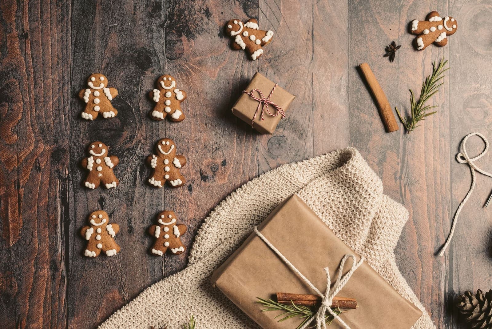 Gingerbread cookies and wrapped presents laid out on a rustic wooden table, seen from above.